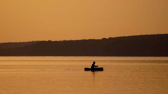 船上渔夫的剪影。日落时从船上在湖上钓鱼