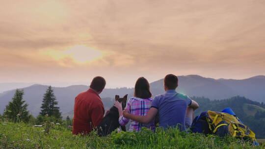 游客和狗坐在山顶看日出