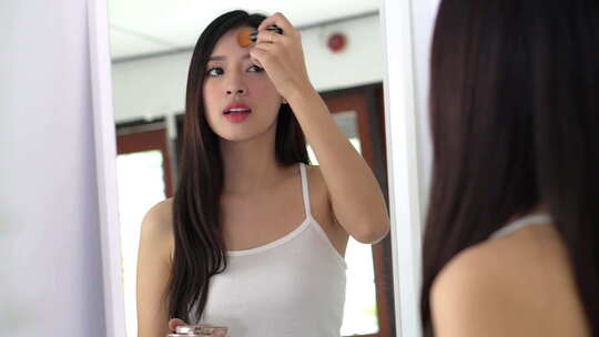 美容肖像亚洲女人用脸颊刷化妆在室内照镜子。