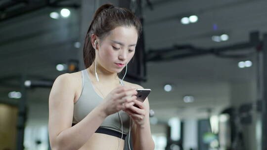 年轻人在健身房健身锻炼休息期间玩手机