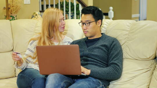 年轻夫妇坐在沙发上看笔记本电脑