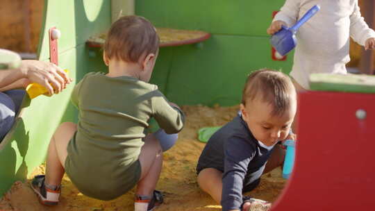 三个蹒跚学步的孩子在沙坑户外玩耍