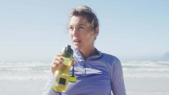 在海滩上喝水的运动妇女视频素材模板下载