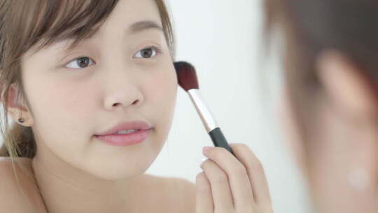 美丽年轻的亚洲女人微笑着用脸颊刷化妆。