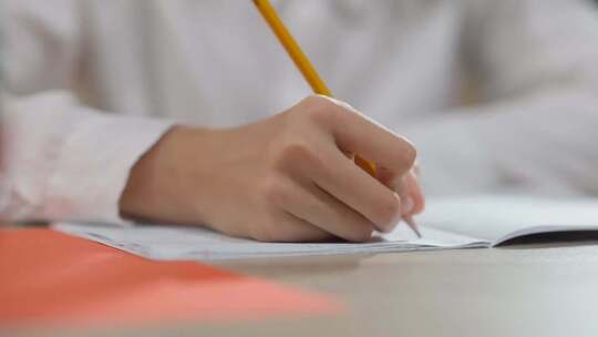学生用铅笔在作业本上书写的手部特写