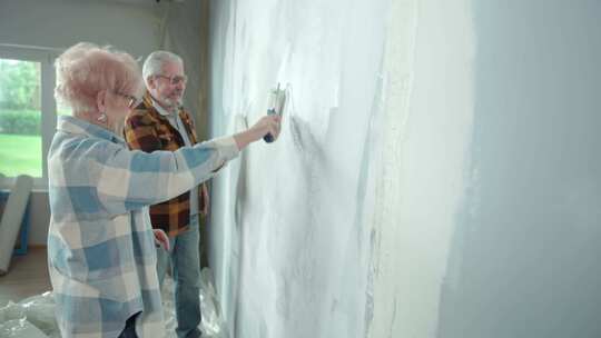 老人和女人正在用油漆滚筒用白色油漆粉刷墙壁