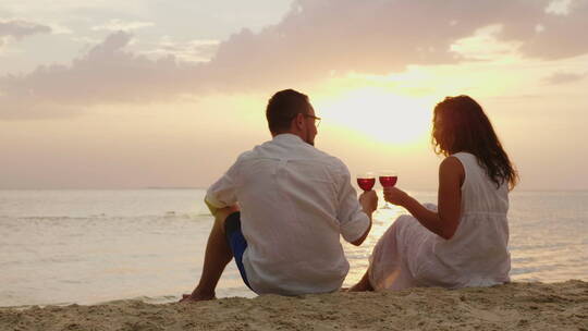 一对年轻夫妇坐在沙滩上喝酒