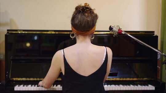 穿着黑色T恤背对着我的女孩弹钢琴
