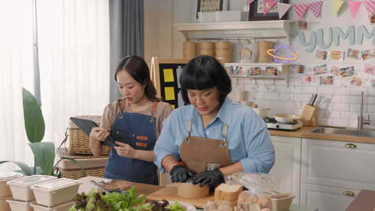 两名亚洲女性在云厨房合作，为在线送餐业务