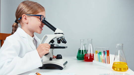 女孩使用显微镜观察实验现象并对着镜头微笑视频素材模板下载