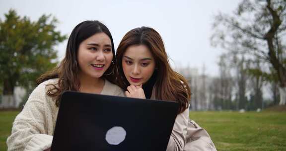 两位年轻美女大学生在校园公园看电脑学习