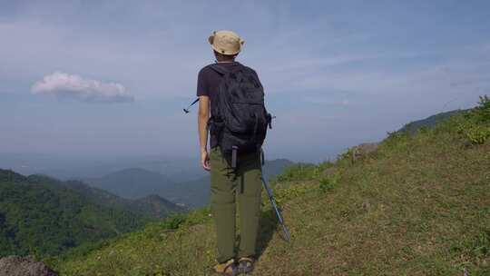 男子山顶背背包持杖眺望远方