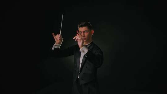 身穿西装的管弦乐团团长使用指挥棒与音乐家