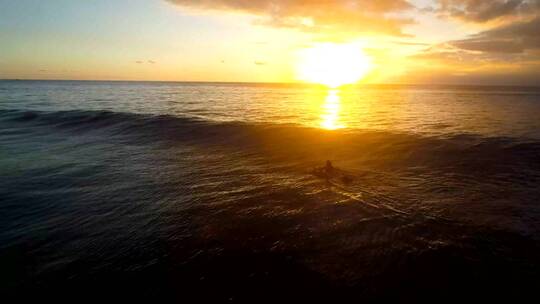 一名女子划着冲浪板越过波浪进入夕阳