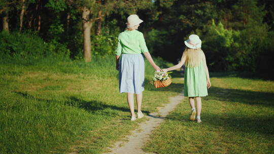 母女拿着一个装有野花的篮子沿着森林里的一条小路走