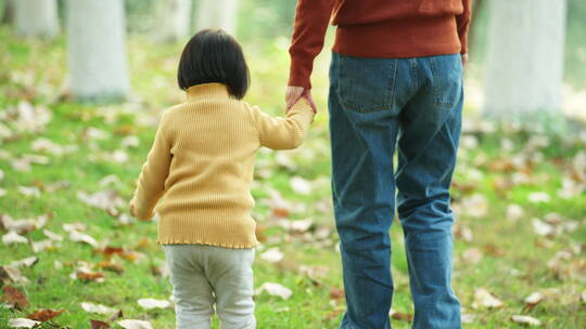 妈妈牵着小女孩的手走在秋天公园草地上