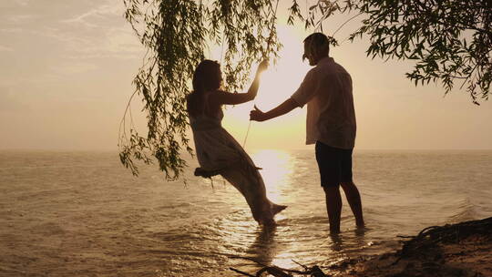 一对年轻夫妇在海边玩秋千