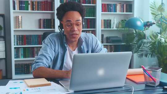年轻的非裔美国人员工远程呼叫中心坐在桌旁，配备笔记本电脑