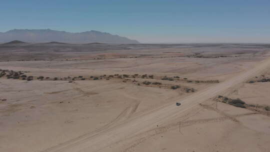 一辆车在沙漠中空旷的砾石路上行驶。
