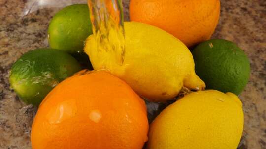 一股水流落在玻璃碗里的柑橘类水果、橙子、柠檬和酸橙上视频素材模板下载