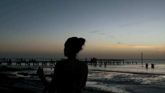 日落美女在海边拿手机拍照参加海滩聚会