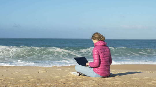 拥有笔记本电脑的自由职业者坐在海滩上