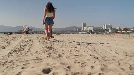 带金属探测器的女性背部在圣莫尼卡海滩的沙