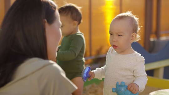 女人在沙盒里和行为不端的蹒跚学步的孩子说话