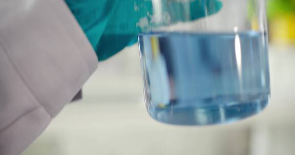 实验人员摇晃观察化学器皿里的蓝色溶液