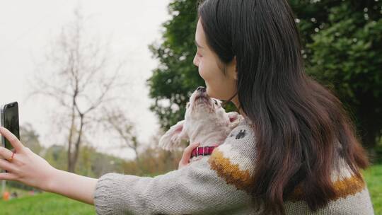 美丽女青年和宠物犬在公园里玩耍用手机自拍