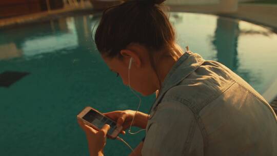 女孩坐在游泳池边发短信