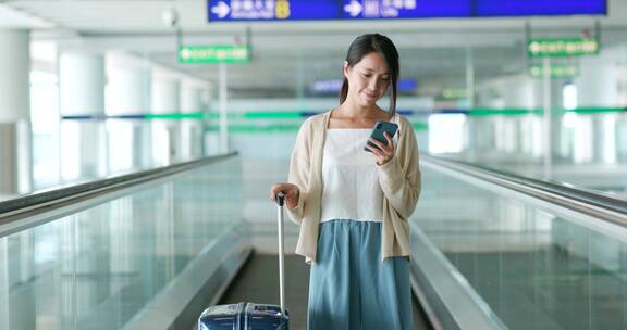 妇女在机场扶梯上使用手机