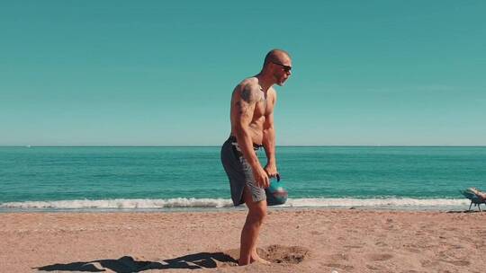 男人在沙滩用壶铃做举重练习