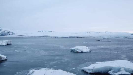 冰山漂浮在白雪覆盖的海岸线上空的海洋中