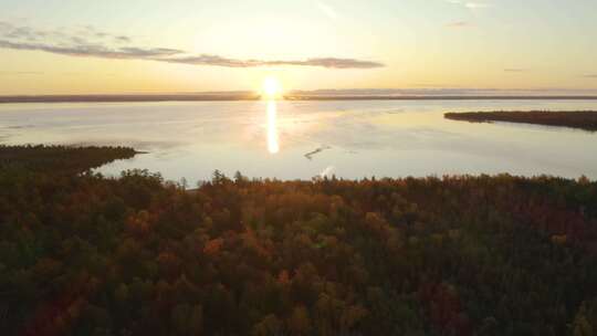 空中撤退，有秋叶的树林，背景是大湖上的日落高清在线视频素材下载