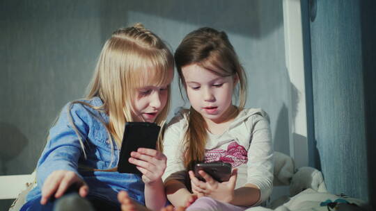两个女孩坐在卧室的床上玩手机