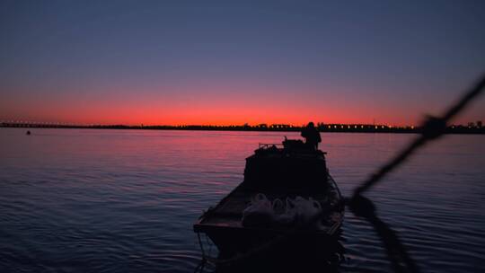 一艘渔船划过黄昏夕阳落日余晖下的松花江