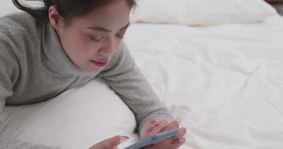 年轻美女开心躺在床上玩手机
