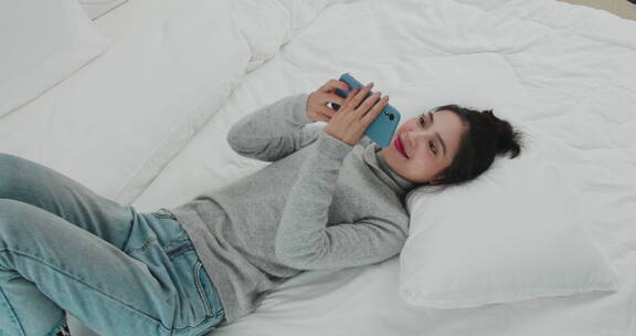 美女躺在床上用手机和远方朋友视频聊天