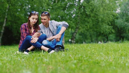 情侣坐在草地上观看手机