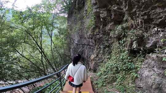 女子沿栈道行走于山林岩石间