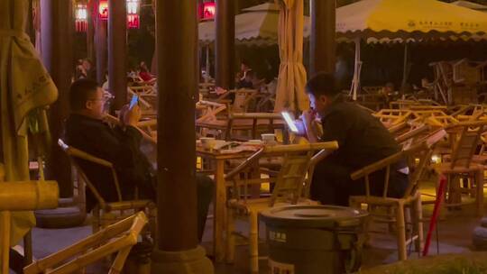 夜晚公园竹编椅喝盖碗茶刷手机的人们视频素材模板下载