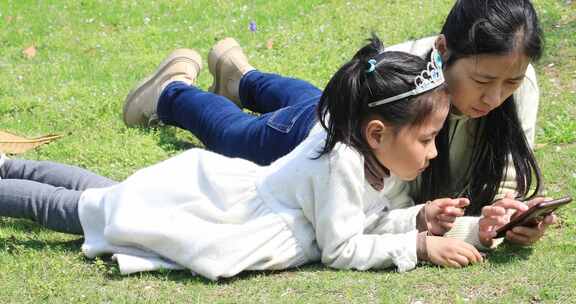 妈妈与女儿开心地趴在草坪上看手机开心微笑