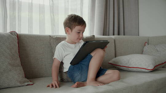 小男孩坐在沙发上玩平板视频素材模板下载