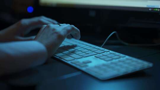 背光黑暗办公室中女性手在键盘上打字的低角度照片