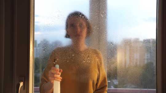 年轻女子在窗户玻璃上喷洒清洁剂一名女子清