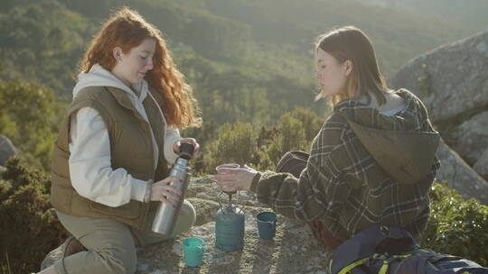 女徒步旅行者坐在山崖上喝热茶