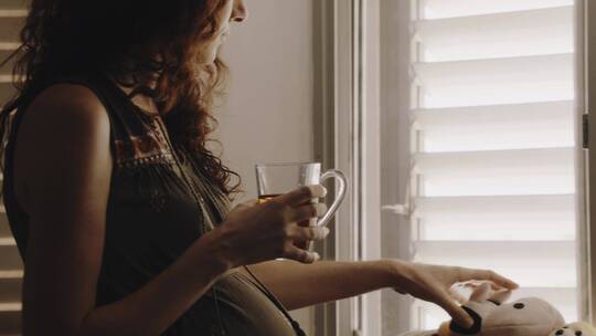 在窗边拿杯子喝水玩玩具的孕妇视频素材模板下载