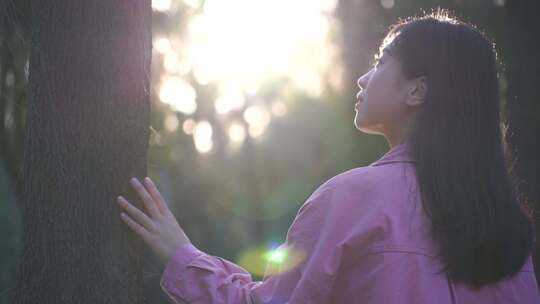 阳光下美女手抚摸树亲近自然感受大自然美好