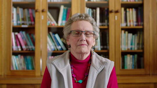 一位老年妇女坐在图书馆里从书架上阅读书籍、小说或文学作品的肖像视频素材模板下载